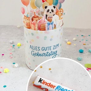 Könnte beinhalten: Eine weiße Geburtstagskarte mit bunten Konfetti und dem Text "Alles Gute zum Geburtstag". Die Karte zeigt Illustrationen von Luftballons, einem Panda und anderen Tieren. Eine Kinder Riegel Schokoriegel liegt im Vordergrund.