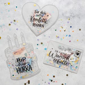 Könnte beinhalten: Drei durchscheinende Acryl-Geschenkhüllen mit buntem Konfetti im Inneren. Eine ist herzförmig mit dem Text "Für dich soll es Konfetti REGNEN", eine ist eine Torte mit drei Kerzen und "Hip hip HURRA", und eine ist ein Umschlag mit "EIN KLEINER Wunscherfüller".