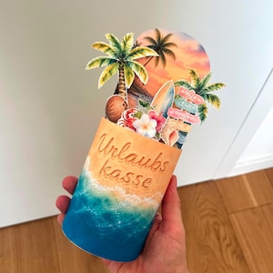 Może przedstawiać: Cylindryczny pojemnik z napisem Urlaubs kasse, przedstawiający plażę z niebieskimi falami i piaskiem. Na górze znajduje się wycięcie z zachodem słońca, palmami, deską surfingową, kokosem, tropikalnymi kwiatami oraz drogowskazami.