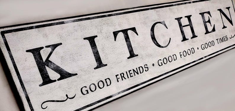 May include: A white wooden sign with black lettering that reads "Kitchen - Good Friends, Good Food, Good Times".