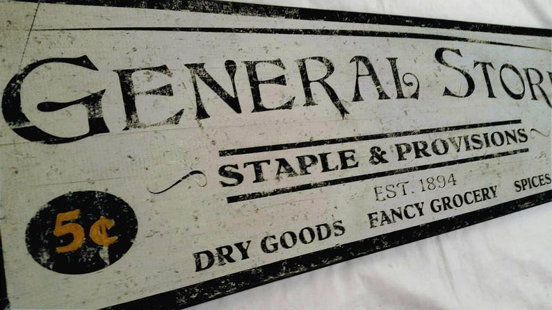 Puede incluir: Un letrero de estilo vintage para una tienda general, pintado en blanco y negro con el texto "GENERAL STORE", "STAPLE & PROVISIONS", "EST. 1894", "DRY GOODS FANCY GROCERY SPICES", y un s&iacute;mbolo de 5&cent;.
