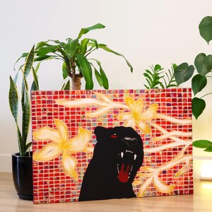 May include: A canvas art piece featuring a black panther with red eyes and an open mouth, set against a red and white checkered background. Yellow floral accents and green plants are also visible.