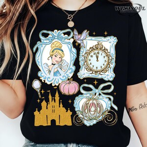 Pode incluir: Camiseta preta com um design temático da Cinderela. O design inclui um retrato da Cinderela, um relógio, uma abóbora, uma carruagem, um castelo e um pássaro, tudo em um esquema de cores azul claro e dourado.