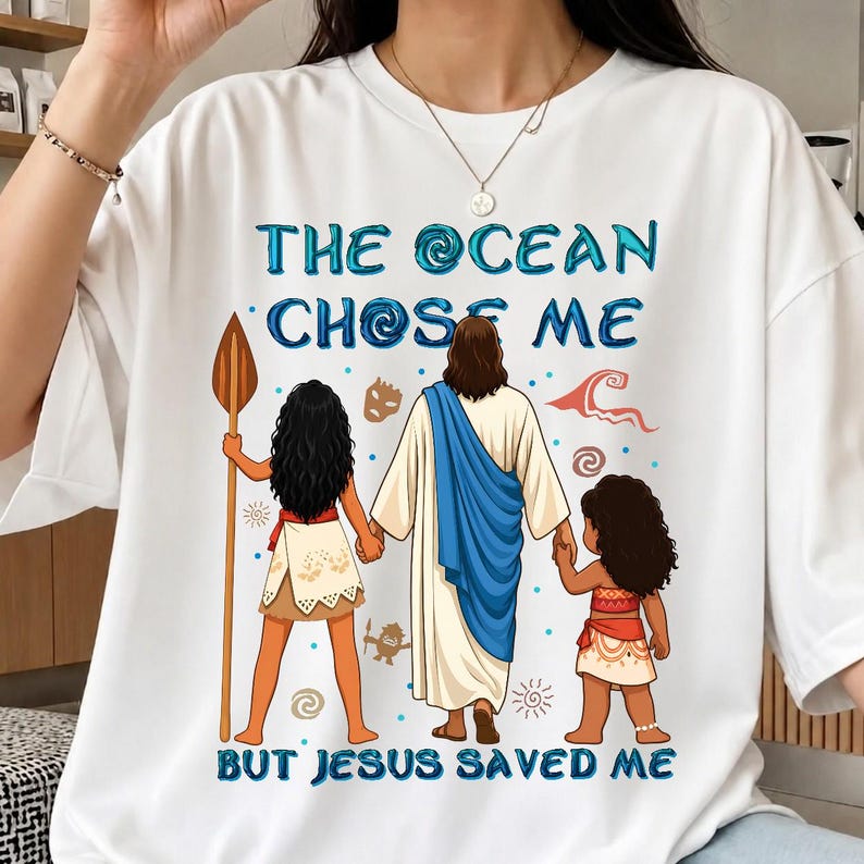 May include: White t-shirt with the text "THE OCEAN CHOSE ME BUT JESUS SAVED ME" in blue. The graphic depicts two girls and Jesus. One girl holds a spear. The other girl is holding Jesus' hand.