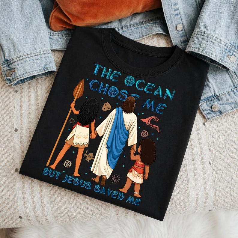 May include: Black t-shirt with the text "THE OCEAN CHOSE ME BUT JESUS SAVED ME" in blue. The shirt features a graphic of Jesus holding hands with two figures, one holding a spear. The figures are in a tropical setting.