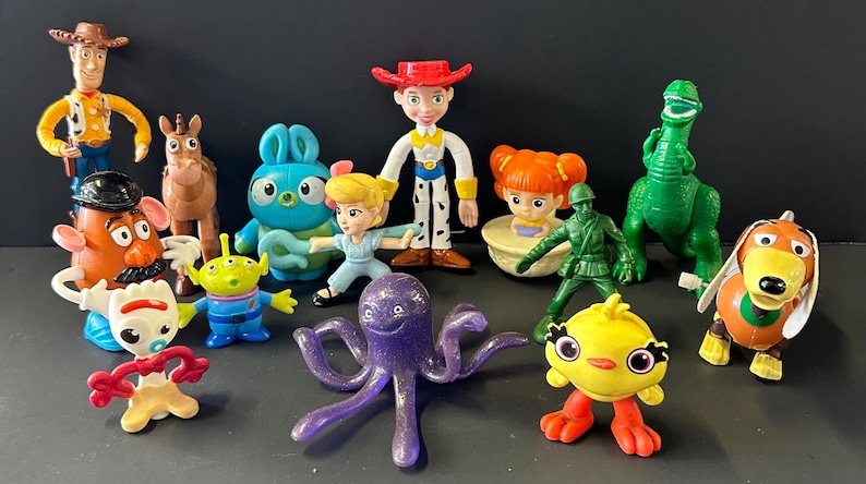 May include: A collection of plastic character figurines including a cowboy, a cowgirl, a green dinosaur, a brown horse, a potato-shaped figure, a blue rabbit, a green alien, a white spork character, a purple octopus, a yellow chick, and a soldier.