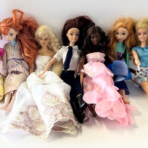 May include: A collection of fashion dolls with various hairstyles and outfits. The dolls include a variety of skin tones and wear dresses, skirts, and tops in colors like yellow, pink, blue, and white. Some dolls have long flowing hair, while others have their hair styled in buns.