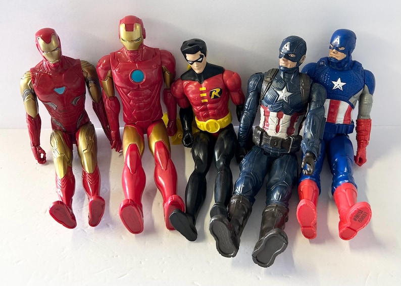 May include: A collection of five superhero action figures, including Iron Man, Robin, and Captain America. The figures are primarily red, gold, blue, and black, with detailed costumes and accessories. They are arranged in a row, showcasing their iconic designs.