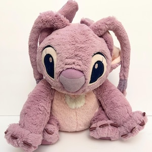 May include: A plush toy of the character Angel from the Lilo & Stitch franchise. The toy is primarily lavender with a light pink chest and inner ears. It has large, dark blue eyes and long, floppy ears.