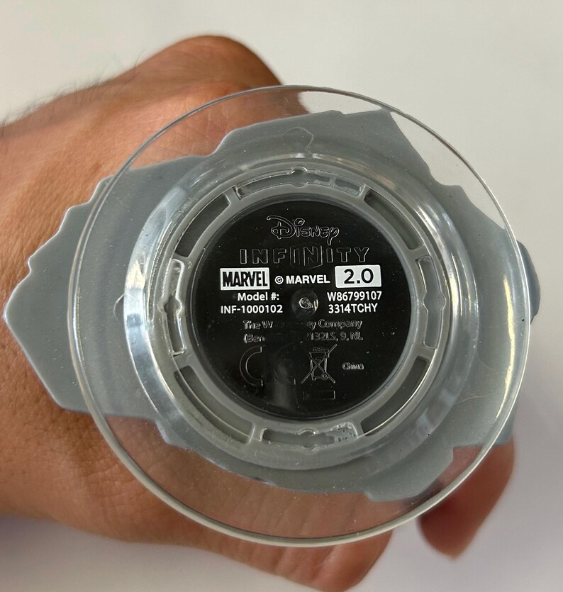 May include: A Disney Infinity Marvel 2.0 base with a clear plastic top. The base is gray with the Marvel logo and model information visible. The text "Disney Infinity" is also present.