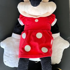 May include: A plush Minnie Mouse doll, featuring a red dress with white polka dots, a matching bow, and white gloves. The doll has black ears, a black nose, and yellow shoes. The toy is designed for children.