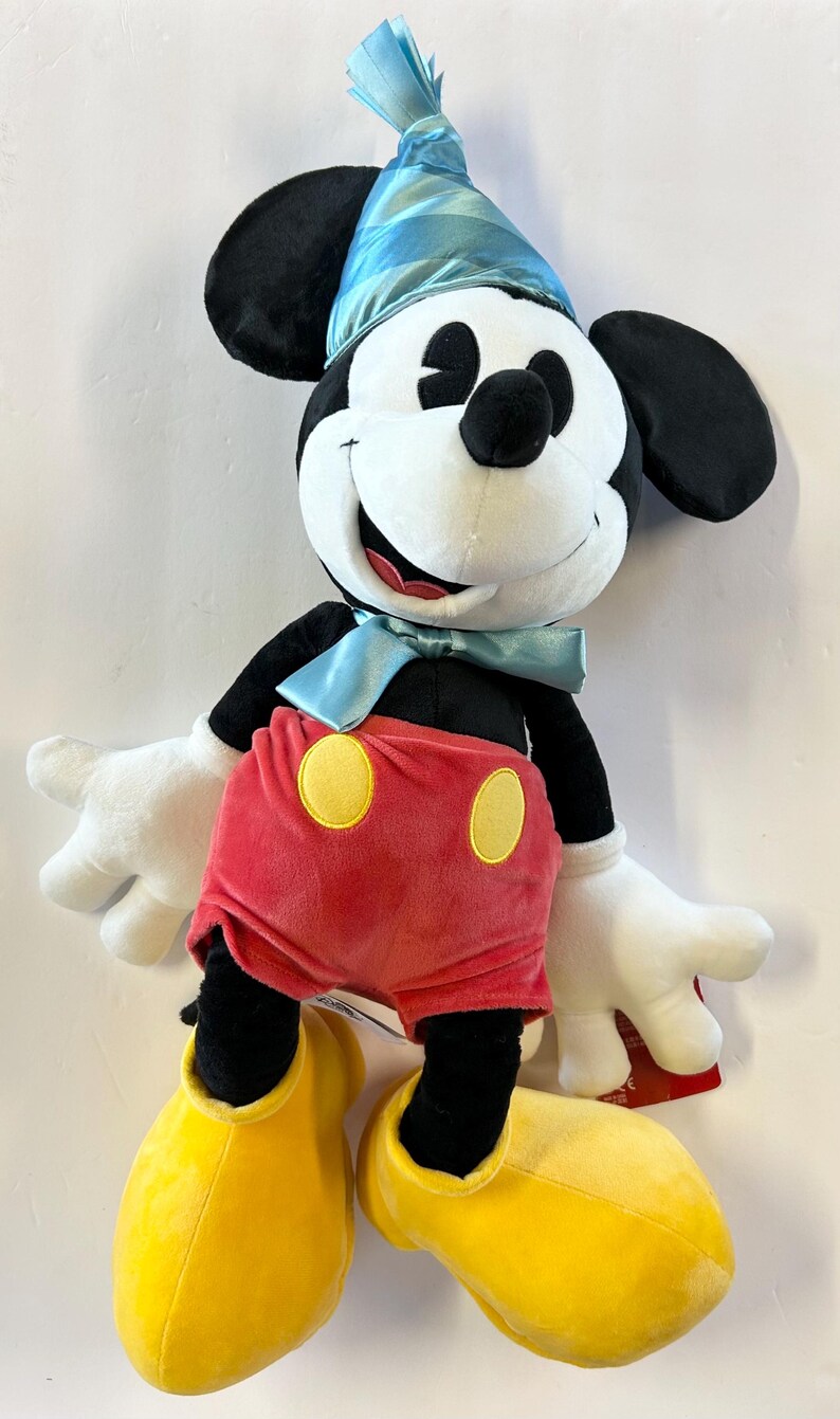 Pu&ograve; includere: Un peluche di Topolino con un cappello da festa blu e un papillon. Topolino ha orecchie nere, viso bianco e pantaloncini rossi con bottoni gialli. Le sue scarpe gialle e i guanti bianchi completano il look.