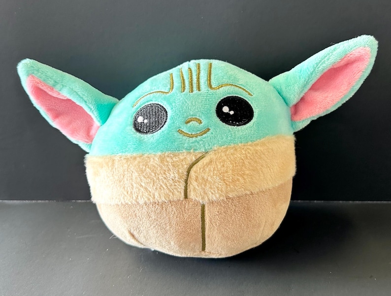 Pode incluir: Um brinquedo de pel&uacute;cia com um personagem com orelhas grandes, olhos pretos e um pequeno sorriso. O brinquedo tem uma cabe&ccedil;a e orelhas verde-claro com o interior das orelhas rosa. A parte inferior &eacute; castanha.
