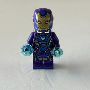 May include: A purple and blue Lego Iron Man figure with a gold mask. The figure has blue energy discs attached to each hand. The figure is standing on a white surface.