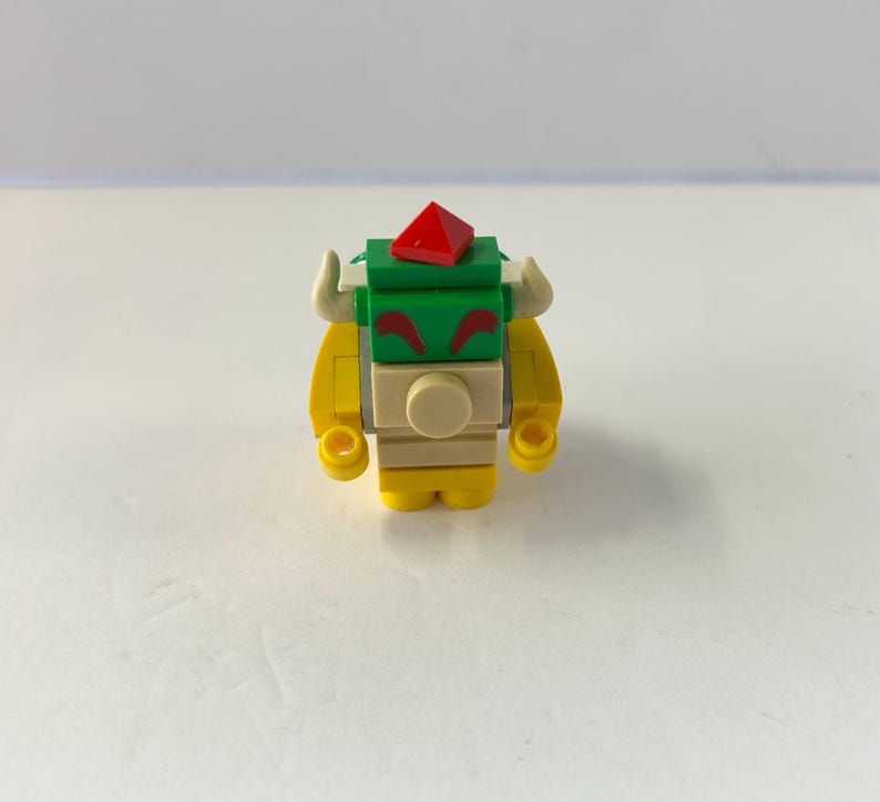 Peut inclure: Une petite figurine Bowser color&eacute;e construite &agrave; partir de briques de jouets embo&icirc;tables. La figurine pr&eacute;sente un corps jaune, une carapace verte et un joyau rouge sur la t&ecirc;te. Elle a des cornes blanches et un visage beige avec des sourcils rouges.
