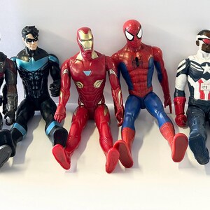 Puede incluir: Se muestran cinco figuras de acci&oacute;n de superh&eacute;roes, incluyendo Iron Man, Spider-Man y Capit&aacute;n Am&eacute;rica. Las figuras est&aacute;n en posici&oacute;n sentada con las piernas extendidas. La paleta de colores incluye rojo, azul, negro y plateado.