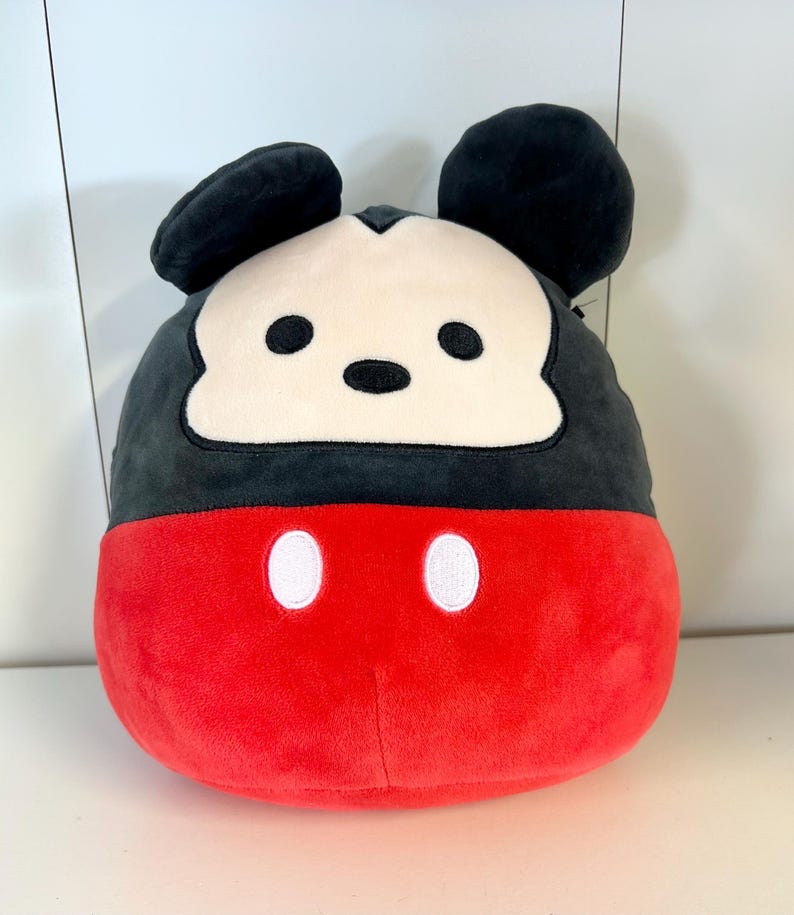 Pu&ograve; includere: Un cuscino rotondo di Topolino. La met&agrave; superiore &egrave; nera con grandi orecchie rotonde. Il viso &egrave; bianco con occhi e naso neri. La met&agrave; inferiore &egrave; rossa con due cerchi bianchi ricamati.