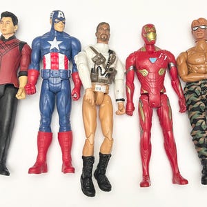 Op de afbeelding: Vijf actiefiguren van superhelden en personages, waaronder Captain America, Iron Man en anderen. De figuren zijn felgekleurd en gedetailleerd, met verschillende kostuums en accessoires. De figuren staan op een wit oppervlak.