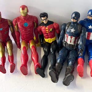 May include: A collection of five superhero action figures, including Iron Man, Robin, and Captain America. The figures are primarily red, gold, blue, and black, with detailed costumes and poses. The figures are made of plastic.