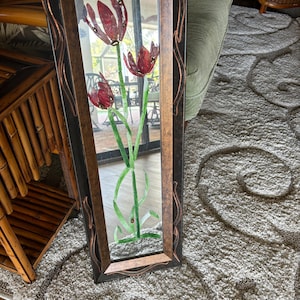 Puede incluir: Un espejo rectangular con un marco de madera oscura y un ribete decorativo de cobre. El espejo tiene un diseño floral con flores rojas y hojas verdes.