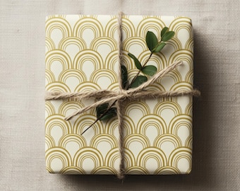 Puede incluir: Un regalo envuelto con papel crema con un patrón de arcos dorados repetidos. El paquete está atado con hilo y adornado con una ramita de hojas verdes, creando una presentación decorativa y elegante.