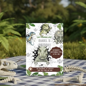 Pu&ograve; includere: Un invito di compleanno a tema dinosauri con illustrazioni di vari dinosauri che sfondano un muro. L'invito include il testo "Let's Celebrate! DANIEL S BIRTHDAY" e i dettagli dell'evento. L'invito &egrave; posto su una coperta da picnic a scacchi.
