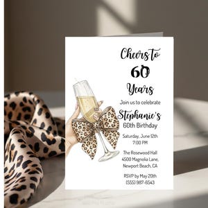 Può includere: Un biglietto d'invito bianco con la scritta "Cheers to 60 Years" e i dettagli per una festa di compleanno per i 60 anni. Il design include un bicchiere di champagne, un fiocco leopardato e informazioni sull'evento.