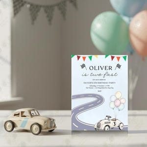 Può includere: Un invito di compleanno con il testo "OLIVER is two fast" e una grafica di auto da corsa a cartoni animati. Un'auto giocattolo è in primo piano e palloncini sullo sfondo. L'invito include i dettagli della festa.