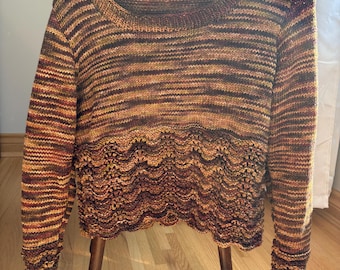 May include: A hand-knitted sweater in shades of brown, gold, and rust, with horizontal stripes across the body and sleeves. The bottom edge features a scalloped, textured design. The sweater is displayed on a wooden hanger.