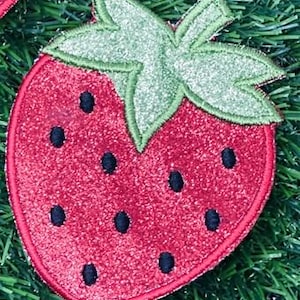 May include: A red glittery strawberry patch with black seed details and a green glittery leaf design. The strawberry is an embroidered patch, perfect for adding to clothing or accessories.