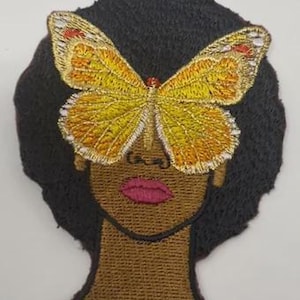 May include: Embroidered patch featuring a woman's face with a butterfly covering the eyes. The butterfly has yellow and gold wings with red accents. The woman's skin is brown, with a pink mouth and black hair.