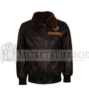 Könnte beinhalten: Braune Leder-Bomberjacke mit Shearling-Kragen und dem Wort "SEAPLANE" auf einem Aufnäher. Die Jacke hat ein Used-Finish, zwei Vordertaschen und schwarze gerippte Bündchen und Saum.