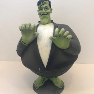 Peut inclure: Buste de Frankenstein vert avec des cheveux noirs, un costume noir et une chemise blanche. La statue a des mains et des pieds verts avec des coutures noires et une cicatrice cousue sur le front. Décoration d'Halloween.