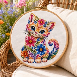 Könnte beinhalten: Ein runder Holzstickrahmen mit einem Kreuzstichmuster eines Kätzchens. Das Kätzchen ist weiß mit orangefarbenen Streifen und mit lebendigen, mehrfarbigen Blumenmustern in Rosa-, Blau- und Gelbtönen verziert.
