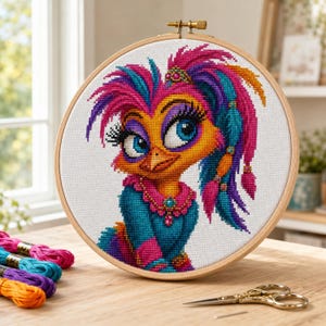Peut inclure: Un tambour à broder circulaire en bois contenant un motif au point de croix représentant un oiseau stylisé aux grands yeux bleus, longs cils et plumage vibrant rose, violet et bleu sarcelle. L'oiseau porte un vêtement bleu sarcelle.