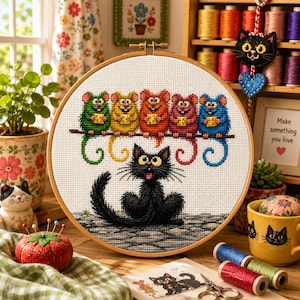 May include: A circular wooden embroidery hoop containing a cross-stitch pattern of five colorful mice sitting on a branch above a black cat. The mice are green, yellow, orange, red, and blue, each holding a small yellow square. The cat is black.