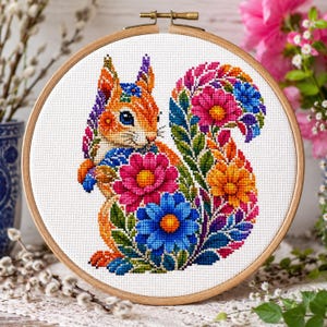 Peut inclure: Un tambour à broder circulaire en bois contenant un motif de point de croix représentant un écureuil. L'écureuil est composé de motifs floraux et de feuilles multicolores aux tons orange, rose, bleu et vert sur un fond en tissu blanc.