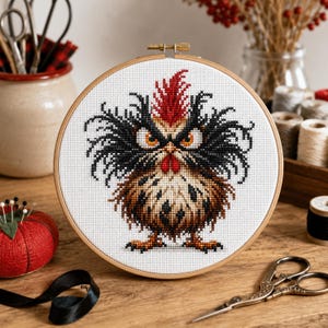 Peut inclure: Un tambour à broder circulaire en bois contenant un motif au point de croix représentant un poulet stylisé à l'air fâché, avec des plumes noires ébouriffées, une crête rouge vif, des yeux orange et un corps tacheté de brun sur fond blanc.