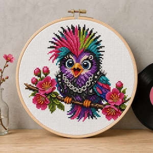 May include: A cross-stitch embroidery in a round wooden hoop featuring a purple owl with a vibrant pink and blue mohawk, wearing a black studded vest and a silver chain necklace, perched on a brown branch with bright pink cherry blossoms.