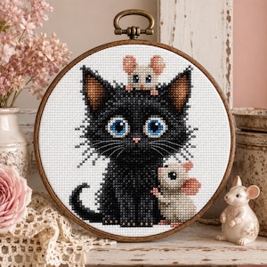 May include: A circular wooden embroidery hoop containing a cross-stitch pattern of a large black cat with bright blue eyes. A small white mouse sits on the cat's head, and another white mouse stands beside the cat's body on a white background.
