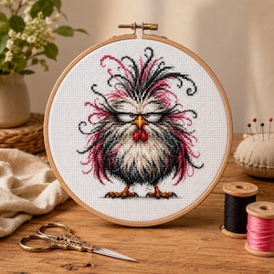Könnte beinhalten: Ein runder Holzstickrahmen mit einem Kreuzstichmotiv eines flauschigen, zerzausten Huhns mit schwarzen und rosa Federn, einem gelben Schnabel und roten Kehllappen. Das Huhn hat einen mürrischen Gesichtsausdruck mit schmalen Augen.