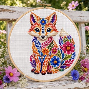 May include: A circular wooden embroidery hoop containing a cross-stitch pattern of a fox. The fox is decorated with vibrant, multi-coloured floral and leaf motifs in shades of orange, blue, pink, and green against a white fabric background.