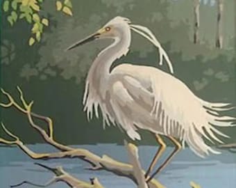 May include: A white egret with a long, slender neck and long legs stands on a branch over a body of water. The egret's feathers are white and fluffy, and its beak is long and yellow. The branch is brown and gnarled, and the water is blue and calm.