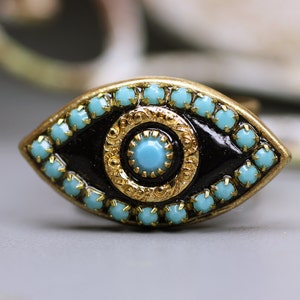 May include: A gold-tone eye charm with a black enamel center and turquoise blue rhinestones around the edge.