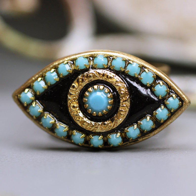 May include: A gold-tone eye charm with a black enamel center and turquoise blue rhinestones around the edge.