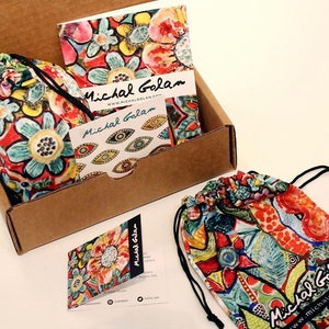 May include: A brown cardboard box containing a colourful patterned fabric bag. The bag has a drawstring closure and is decorated with a floral design. The box also contains a small card with the text "Michal Golan" and a website address.