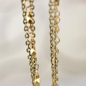 May include: Two gold chains with geometric beads hanging against a white background.