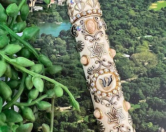 May include: A white and gold decorative mezuzah with a Star of David, a menorah, and other ornate details. The mezuzah is adorned with rhinestones and pearls.