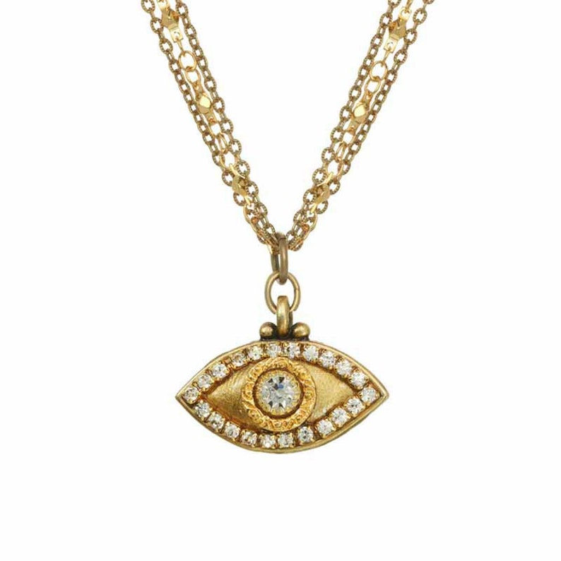 May include: Gold necklace featuring a diamond-encrusted evil eye pendant. The pendant is a detailed, stylised eye with a single, larger diamond in the centre.