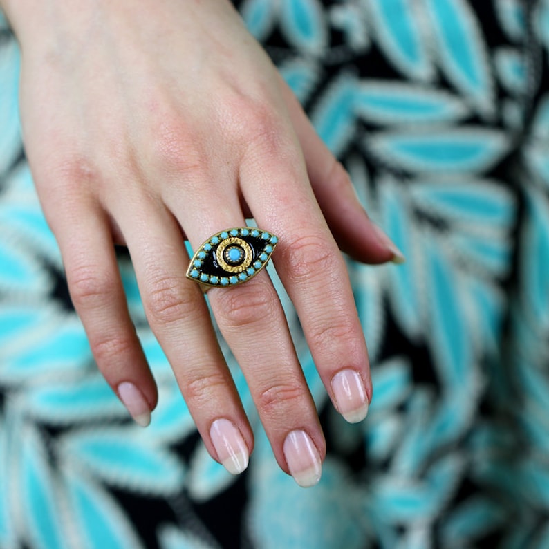 May include: A gold ring with a blue and black evil eye design. The ring is set with turquoise stones and has a gold border.